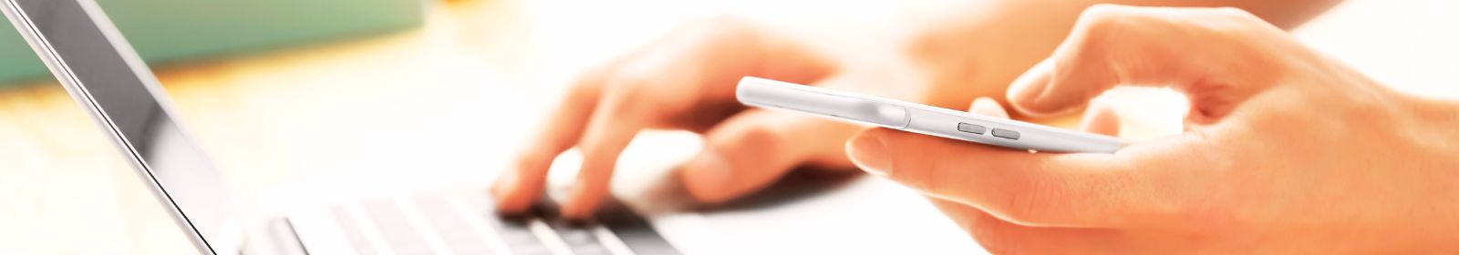 Person holding a cell phone and typing on their laptop.